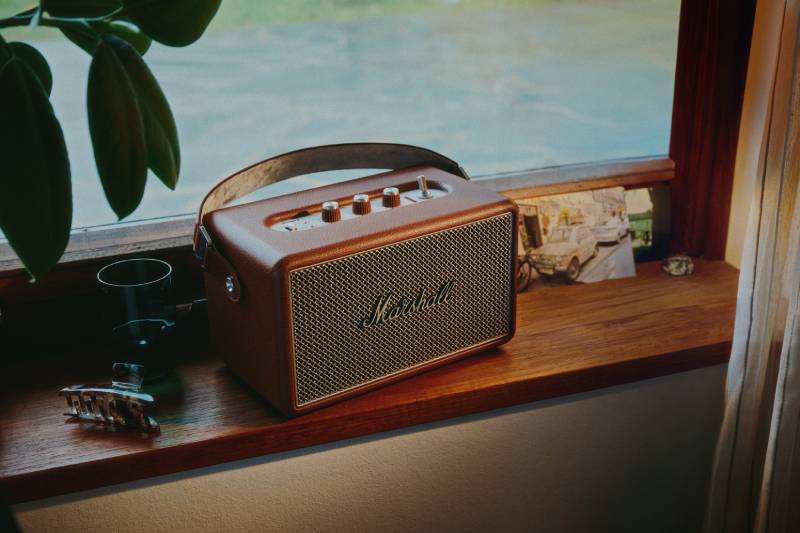 Dispositivo de audio con diseño clásico colocado sobre una repisa de madera, acompañado por objetos decorativos y una iluminación suave que resalta su estética retro.