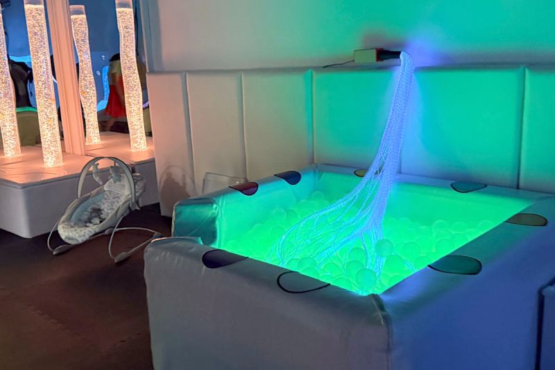 Espacio sensorial con piscina de pelotas iluminada y elementos de estimulación visual.