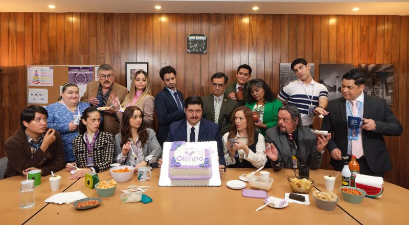 La Oficina — Celebración en Jabones Olimpo Un grupo de empleados celebra alrededor de una mesa en una oficina, con pastel, comida y ambiente festivo, evocando el tono humorístico y cotidiano de la serie.