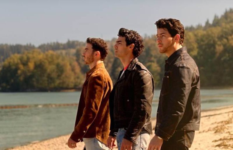 El regreso de Connect 3 con los Jonas Brothers Nick, Joe y Kevin Jonas parados en perfil frente a la playa con chamarras de piel y anteojos de sol, mirando reflexivos hacia el horizonte.