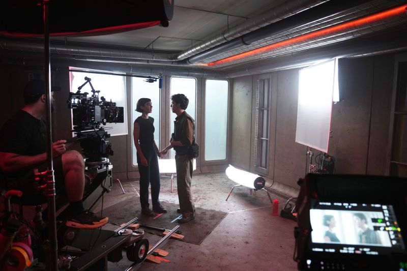 Equipo de filmación capturando una escena entre dos actores en un set con iluminación profesional y cámaras de cine.