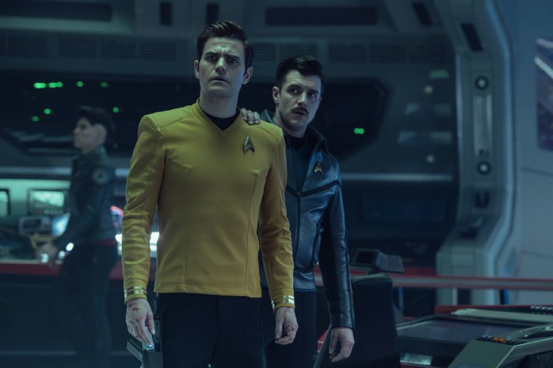 Tres integrantes de una tripulación espacial en una sala de mando futurista, rodeados de paneles y controles tecnológicos.