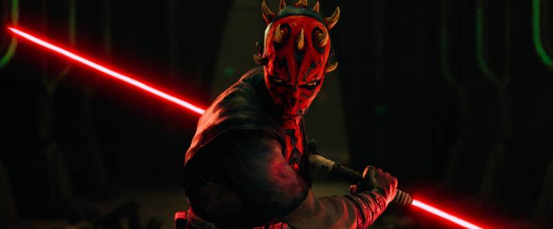 Maul en Star Wars: Lord de las Sombras Personaje de piel roja y negra con cuernos y un sable de luz doble encendido, en un entorno oscuro con arquitectura futurista iluminada en tonos verdes.