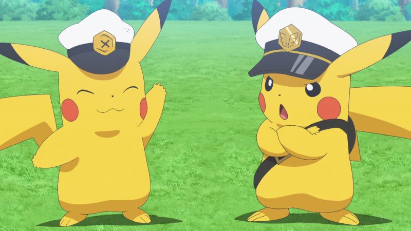Fotograma de la serie Horizontes Pokémon. En un entorno natural de pradera verde y arbolada aparecen dos Pikachu vistiendo gorras de capitán blancas con insignias doradas. El Pikachu de la izquierda sonríe amistosamente levantando una pata, mientras que el Pikachu de la derecha adopta una postura desafiante con los brazos cruzados y una pequeña mochila cruzada al hombro.