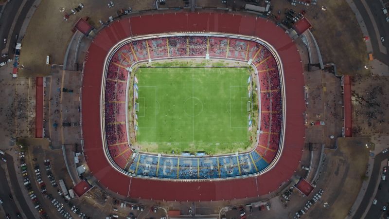 Toma cenital aérea de la cancha de fútbol del Estadio Corregidora rodeada por las tribunas durante un partido.