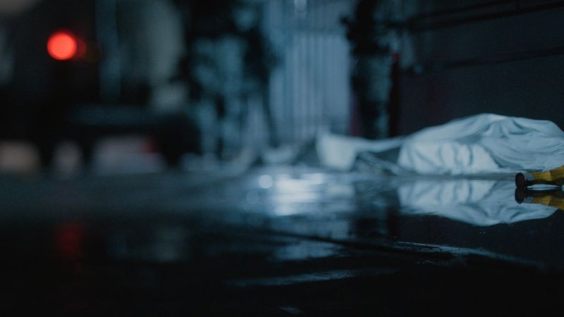 Plano detalle en ambiente oscuro con luz azul mostrando objetos tirados en el suelo y marcadores de evidencia policial.