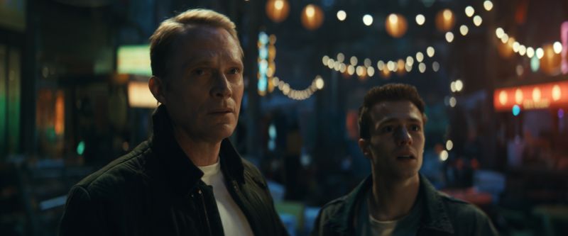 Paul Bettany junto a Ruaridh Mollica como Tommy Shepard observando sorprendidos en una calle iluminada por luces nocturnas.