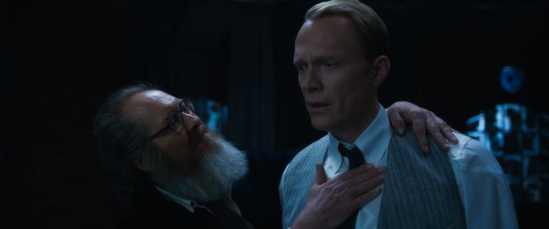 James Spader en su avatar humano con barba gris y anteojos colocando una mano sobre el pecho de Paul Bettany.