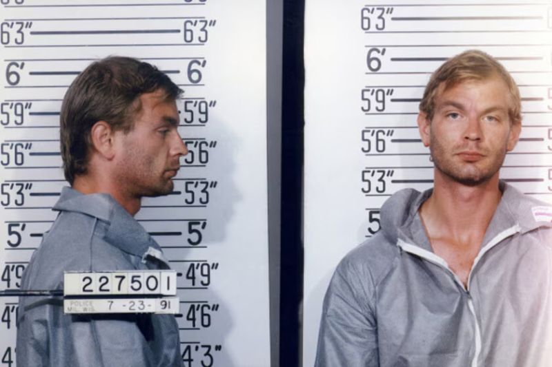 Ficha policial de Jeffrey Dahmer para el documental en A&E Fotografía de ficha policial de Jeffrey Dahmer en vista lateral y frontal vestida con uniforme gris de prisión frente a una escala de estatura.