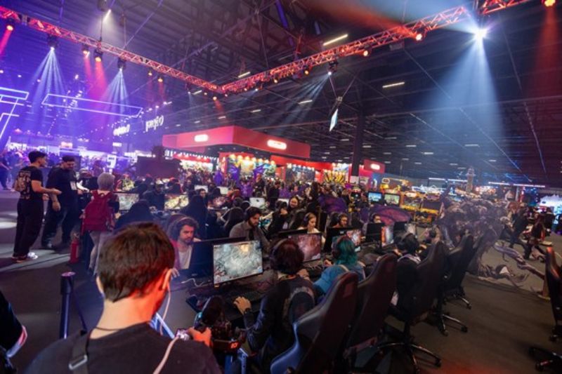 Brasil Game Show 2026 — Preventa Área de un evento gamer con estaciones de juego, público participando y luces de escenario en tonos azules y rojos.