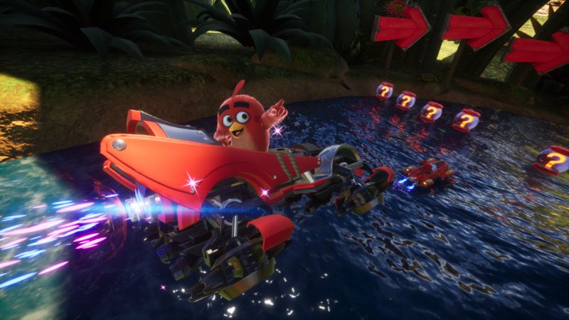 Sonic Racing: CrossWorlds x Angry Birds Personaje rojo estilo ave conduciendo un vehículo futurista sobre agua en un entorno colorido con elementos de carrera y cajas flotantes.
