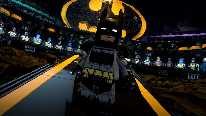 Figura de LEGO Batman en un entorno que representa la Baticueva, con vitrinas iluminadas que exhiben trajes y un símbolo del murciélago en el fondo.