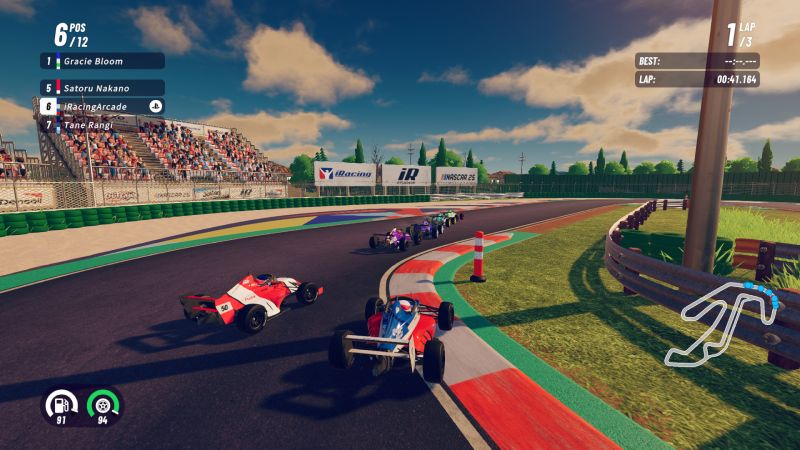 Carrera de monoplazas en iRacing Arcade para PS5 Captura de pantalla de una carrera en el videojuego iRacing Arcade tomada desde la consola PlayStation 5. La toma muestra una curva cerrada de un circuito de carreras con vista trasera en tercera persona. Varios monoplazas coloridos estilo Fórmula compiten sobre el asfalto junto a los pianos rojos y blancos. Al fondo se observa una grada llena de espectadores, espectaculares de patrocinadores como iRacing y NASCAR 25, árboles y un cielo despejado con nubes. En las esquinas superiores se despliega la interfaz con posiciones de carrera (como Gracie Bloom, Satoru Nakano y Tane Rangi) y tiempos de vuelta, mientras que en la esquina inferior izquierda se aprecian los medidores de combustible y neumáticos.