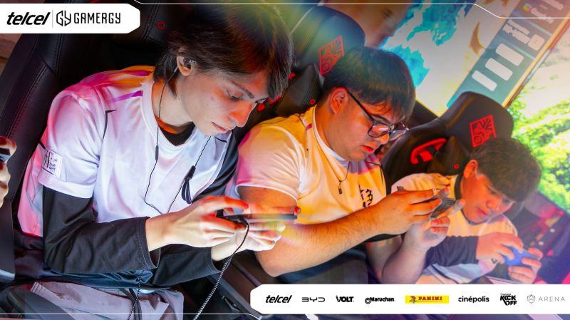 Fotografía en toma media de tres jugadores jóvenes de esports sentados en sillas gamer de la marca OMEN mientras compiten concentrados sosteniendo sus teléfonos móviles de forma horizontal durante un torneo presencial. Portan camisetas oficiales de competencia en tonos blanco, violeta y negro con audífonos in-ear conectados a los dispositivos. En la esquina superior izquierda se ubica el logotipo de Telcel GAMERGY, mientras que en la franja inferior blanca aparecen las insignias de los patrocinadores oficiales como Telcel, BYD, Volt, Maruchan, Panini, Cinépolis, Concacaf Kick-Off y Arena.