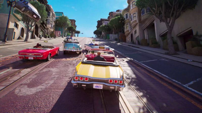 Captura de pantalla de jugabilidad de Crazy Taxi: World Tour. Muestra una amplia avenida inclinada al estilo de San Francisco en un día soleado, donde cuatro descapotables clásicos de colores amarillo, rojo y azul compiten a toda velocidad cuesta abajo. A la izquierda, un automóvil negro sale volando por los aires entre los árboles y edificios tras una colisión.