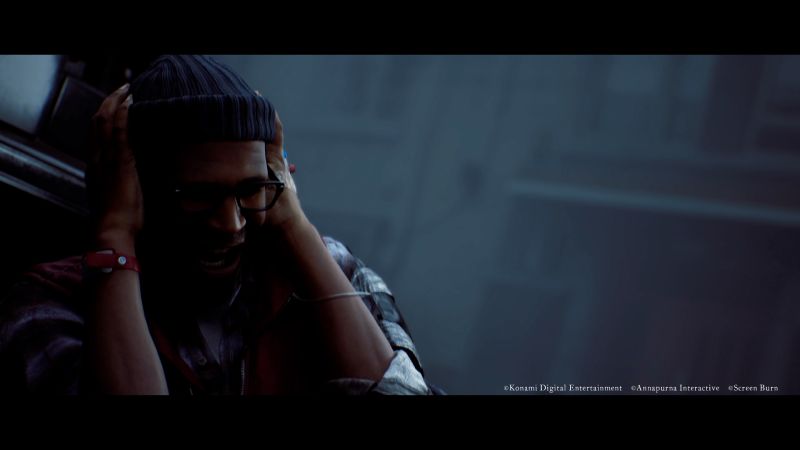 Captura del tráiler de SILENT HILL: Townfall en resolución 4K. Un hombre de tez morena (Simon Ordell) viste un gorro azul de lana, lentes de armazón negro y una camisa a cuadros. Se encuentra gritando angustiado mientras se cubre las orejas con ambas manos con fuerza, envuelto en una atmósfera oscura, húmeda y con niebla pesada de fondo.