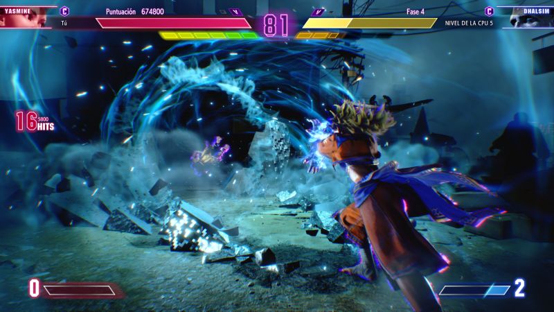 Super Art de Yasmine en Street Fighter 6 Captura de pantalla de combate mostrando el clímax visual de un Super Art de Yasmine con destellos de energía azul, polvo y escombros proyectados mientras ataca a Dhalsim.