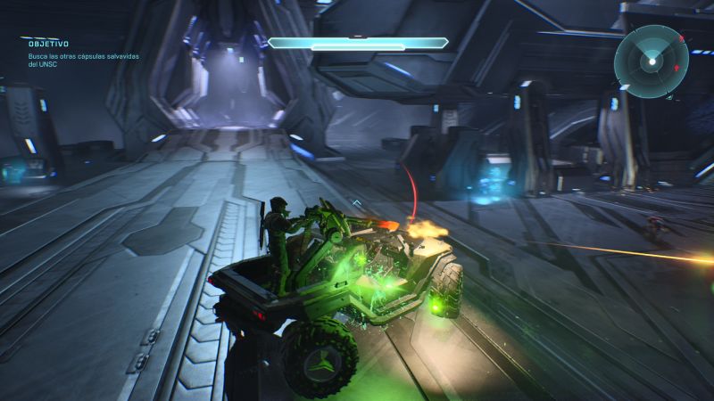 Acción vehicular a bordo del Warthog en Halo: Campaign Evolved Vista en tercera persona de un vehículo Warthog verde siendo conducido dentro de un pasillo industrial iluminado con chisporroteos y efectos de disparos en el chasis.