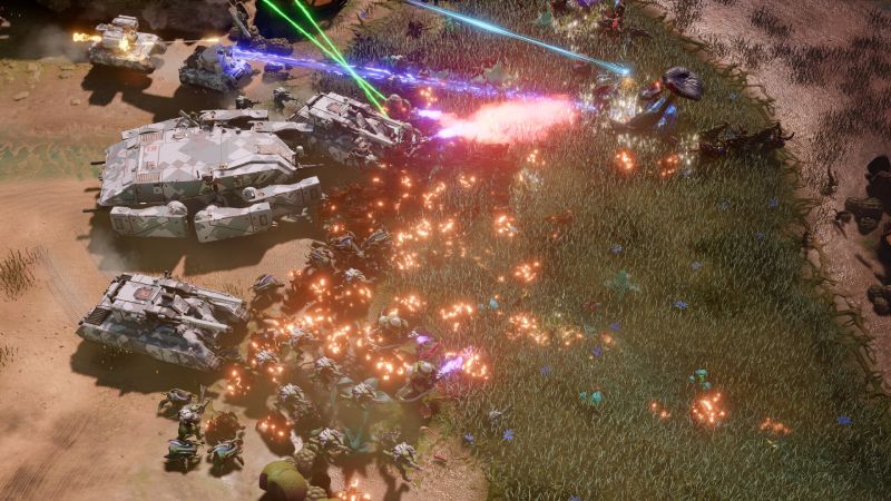 Vista superior de una intensa batalla RTS donde tanques futuristas disparan láseres azules y rosas contra una horda de criaturas alienígenas en un bioma selvático.