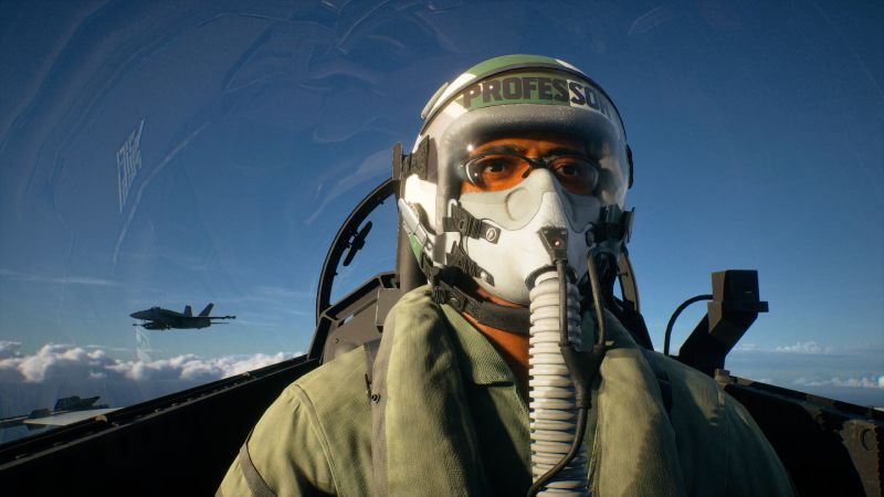 Fotografía de un piloto dentro de la cabina de un avión de combate, con otro jet volando a distancia sobre un cielo despejado.