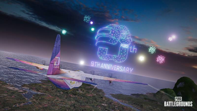 Aeronave decorada con colores festivos sobrevolando una costa al atardecer, acompañada por fuegos artificiales y un despliegue de drones que forman un logotipo alusivo al noveno aniversario del juego.