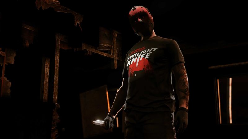Un personaje de GTA Online posa en un entorno oscuro y tenebroso vistiendo una máscara de hockey roja con orificios estilo Slashing y una camiseta negra con la inscripción "TWILIGHT KNIFE" sobre una ilustración de un asesino de película de terror. En su mano derecha sostiene un cuchillo con la hoja brillante.   