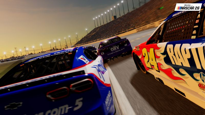 Carrera nocturna en NASCAR 26 Captura de pantalla del videojuego NASCAR 26 que muestra varios autos de carreras compitiendo a alta velocidad sobre un óvalo durante el atardecer. En primer plano destaca un auto con el número 24 y patrones de llamas, seguido por un vehículo azul con el número 5 y un auto morado con el número 48 bajo la iluminación de los reflectores del circuito.