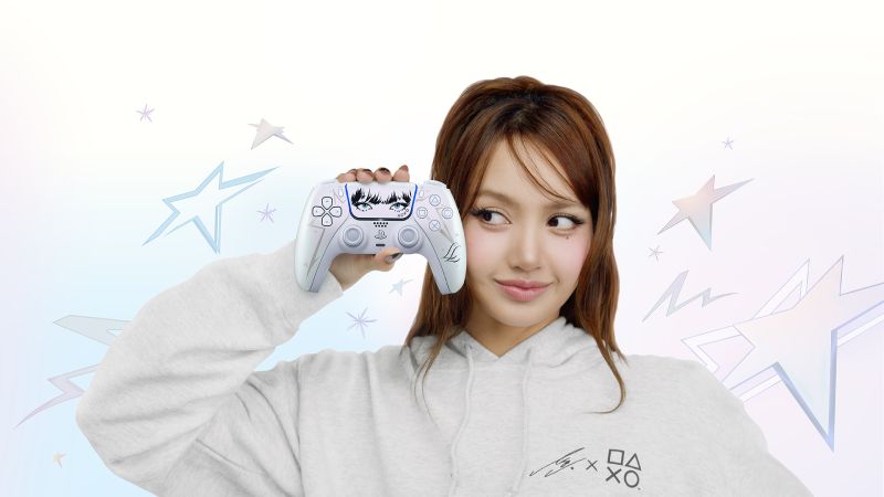 La cantante e ícono de K-Pop LISA sosteniendo el nuevo control inalámbrico DualSense Edición Limitada frente a su rostro. El control presenta un diseño blanco perlescente Chroma Pearl con ilustraciones negras en el touchpad de sus ojos y flequillo, y letras LL en las empuñaduras, rodeada de ilustraciones de estrellas brillantes.